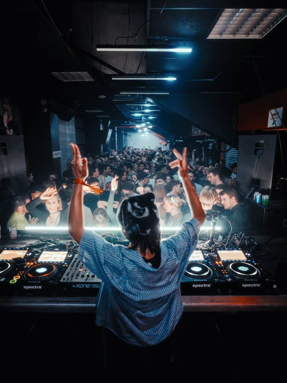 Le DJ bras levés face au public, coursive en perspective